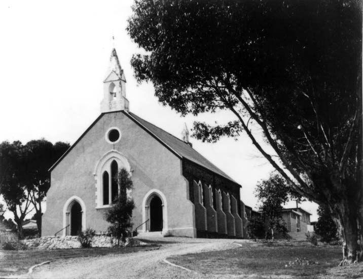 Black-and-white photograph of the rendered Baptist church from the side, showing the gable front with steeple, round window, Gothic arched windows along the nave, and a gum tree to the right