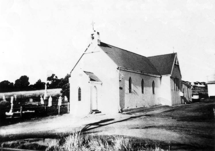 Black-and-white photograph of the rendered St Mary's Church — a pointed steeple, Gothic arched windows on the nave, and a cemetery with headstones behind a fence to the left