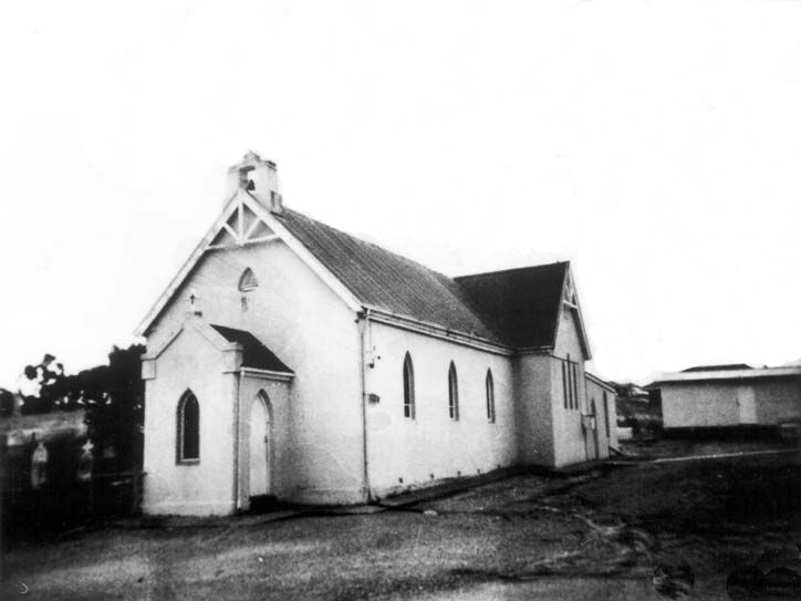 Black-and-white photograph of the rendered St Mary's Church from the side — the gable front with bellcote and cross, a Gothic arched doorway with porch, and lancet windows along the nave