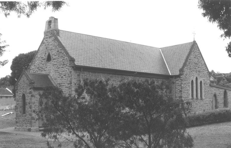 Black-and-white photograph of the restored original St Mary's Catholic Church — a coursed stone building with Gothic arched windows, slate roof, small bellcote, and a native shrub in the foreground