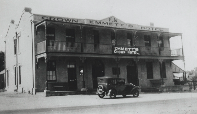 Black-and-white photograph of a two-storey rendered hotel with the sign Emmett's Crown Hotel and a vintage car parked outside