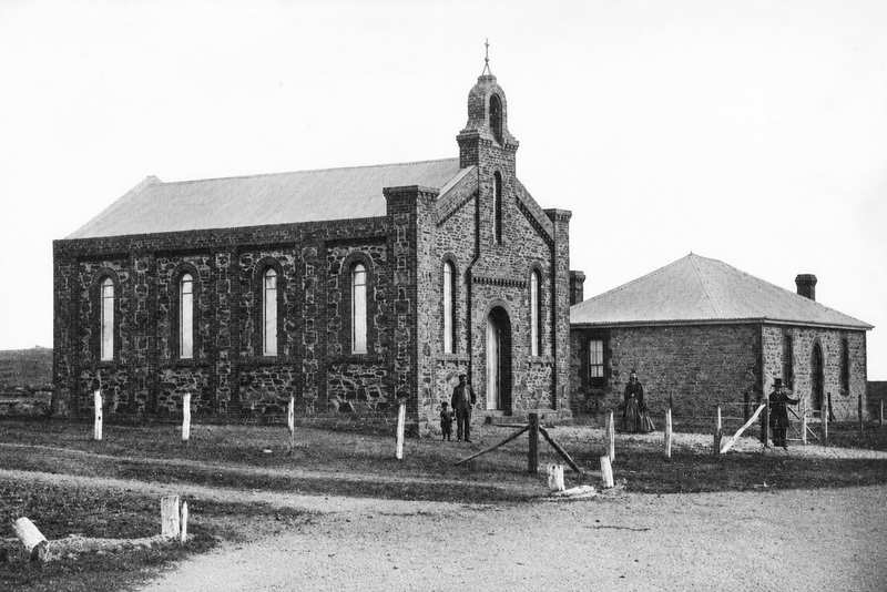 Black-and-white photograph of the Happy Valley Congregational Church — a stone church with Gothic arched windows, bellcote, and arched doorway; figures outside and a stone schoolroom adjacent to the right