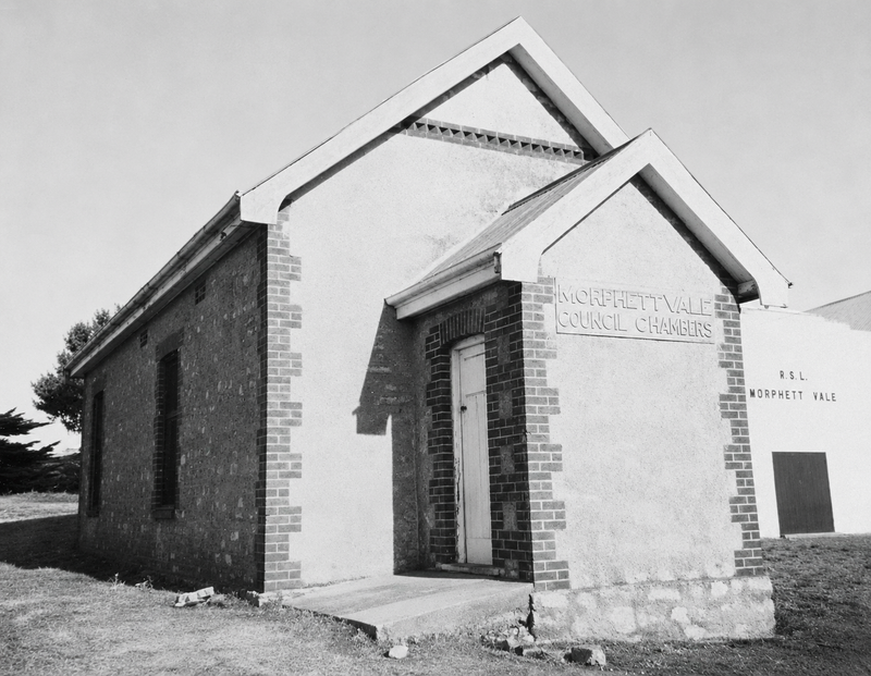Black-and-white photograph of a small rendered stone building with Morphett Vale Council Chambers lettered on the facade, the Morphett Vale RSL visible adjoining it on the right