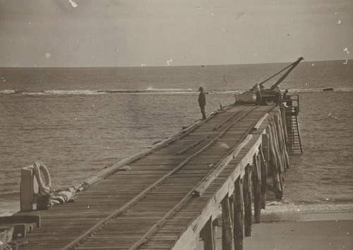 Sepia photograph taken from Port Noarlunga jetty looking toward shore, a lone man standing on the timber deck with the jetty trestle structure beside him