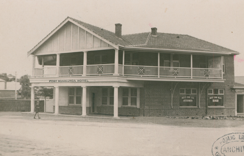 Black-and-white photograph of the Port Noarlunga Hotel, a two-storey timber building with ornate verandah railings on both levels, on an unpaved road