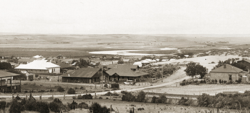 Sepia panoramic photograph of Port Noarlunga from a hilltop, looking across scattered houses toward the flat coastal plain and sea in the distance