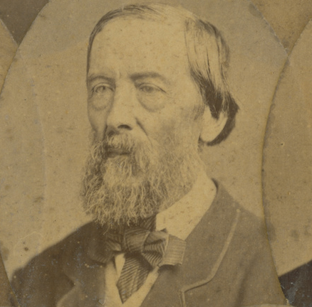 Sepia studio portrait of a middle-aged man with a full beard and moustache, wearing a dark jacket and bow tie, facing slightly right, cropped in an oval vignette in the carte-de-visite style