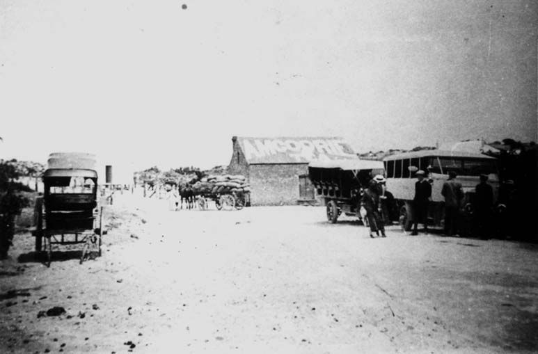 Black-and-white photograph of a Port Noarlunga coastal scene around 1920 — a shop with tea rooms signage, a horse-drawn wagon, and an early motor bus on a sandy street