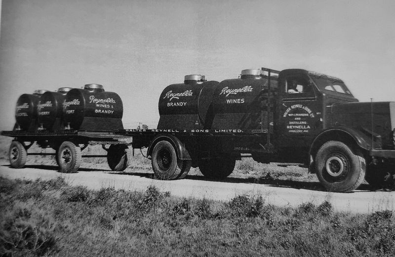 Black-and-white photograph of a Walter Reynell and Sons bulk wine tanker truck pulling a trailer with multiple barrel-shaped tanks labelled Reynella Wines and Brandy on a country road
