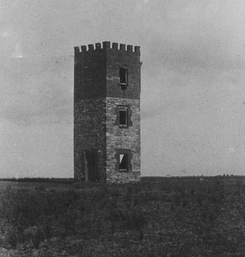 Black-and-white photograph of the Castle tower at White's Valley — a square three-storey stone tower with crenellated battlements at the top, standing alone in a flat open paddock, windows on each floor