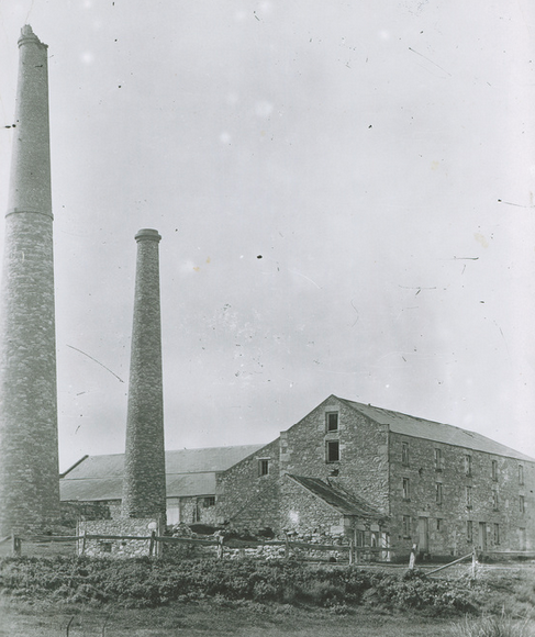 Black-and-white photograph of White's Flour Mill at White's Valley — two chimney stacks of unequal height rising above a two-storey stone mill building, with low stone structures in the foreground