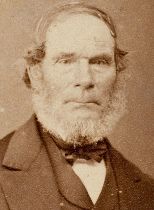 Sepia-toned studio portrait of an elderly man with a full white beard, wearing a dark coat and bow tie, facing slightly left