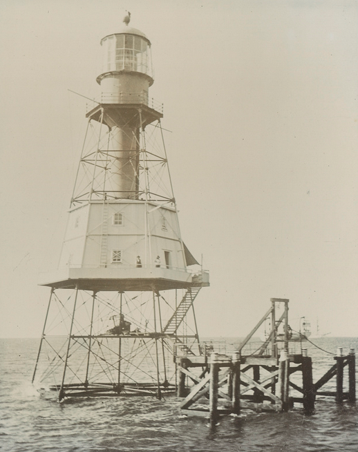 Sepia photograph of the Wonga Shoal Lighthouse standing in open water — a tall cylindrical tower with a lantern room on top and an open lattice platform at the base, with a landing stage extending from it
